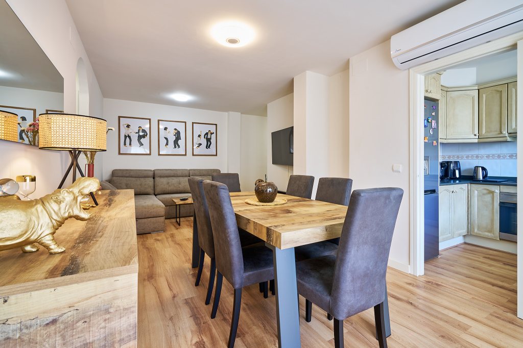 Elegante y confortable comedor con mesa de madera para 6 comensales y salón de estar con televisión con entrada en la cocina